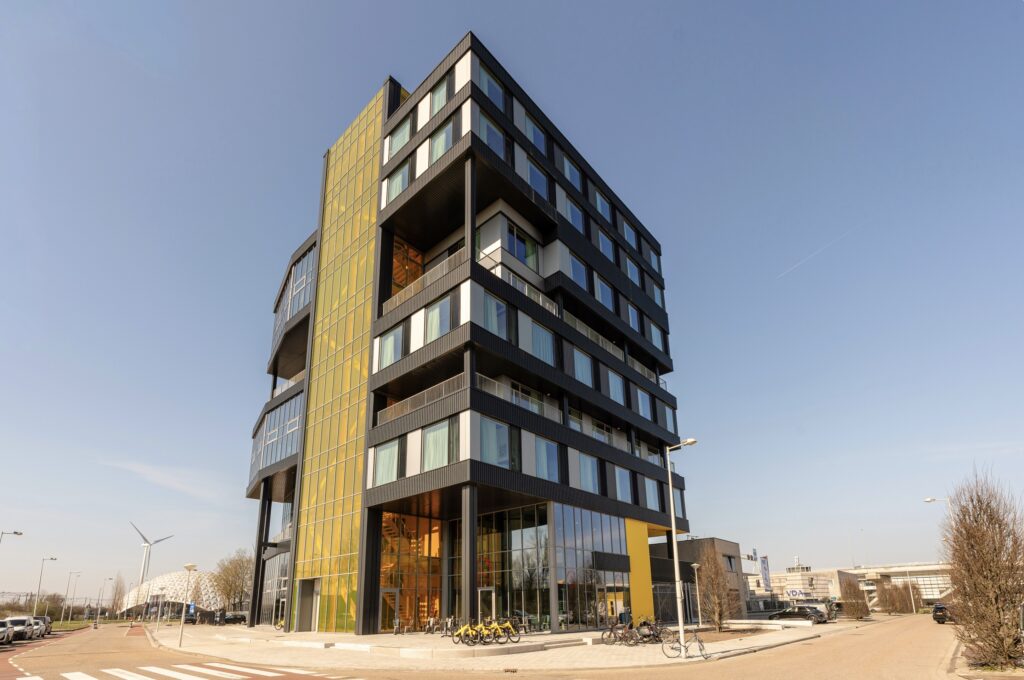 Short stay or hotel room in Amsterdam, what's the difference? Exterior of Makerstoren Amsterdam Sloterdijk, a striking ten-storey building with gold and dark facade, balconies and glass facade on the ground floor