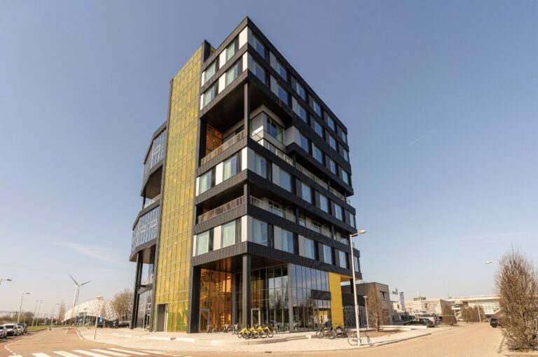Exterior of Makerstoren Amsterdam Sloterdijk, a striking ten-storey building with gold and dark facade, balconies and glass facade on the ground floor