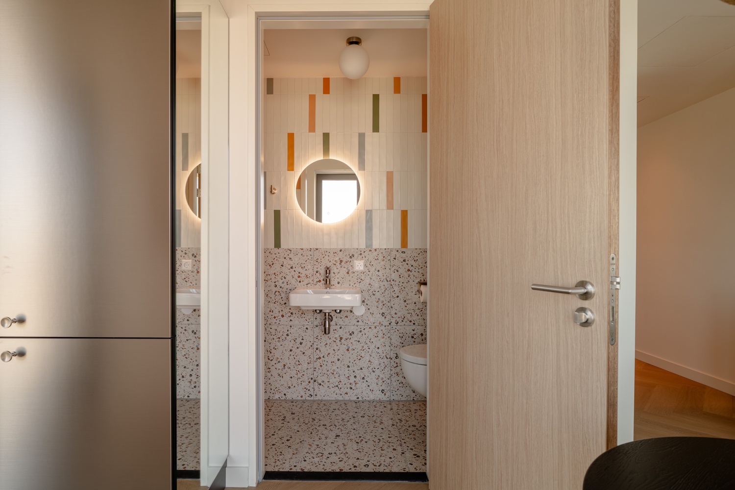 Doorkijk vanuit de hal naar de en-suite badkamer van de Superior Studio with Balcony in Makerstoren, met kleurrijke tegels en terrazzo