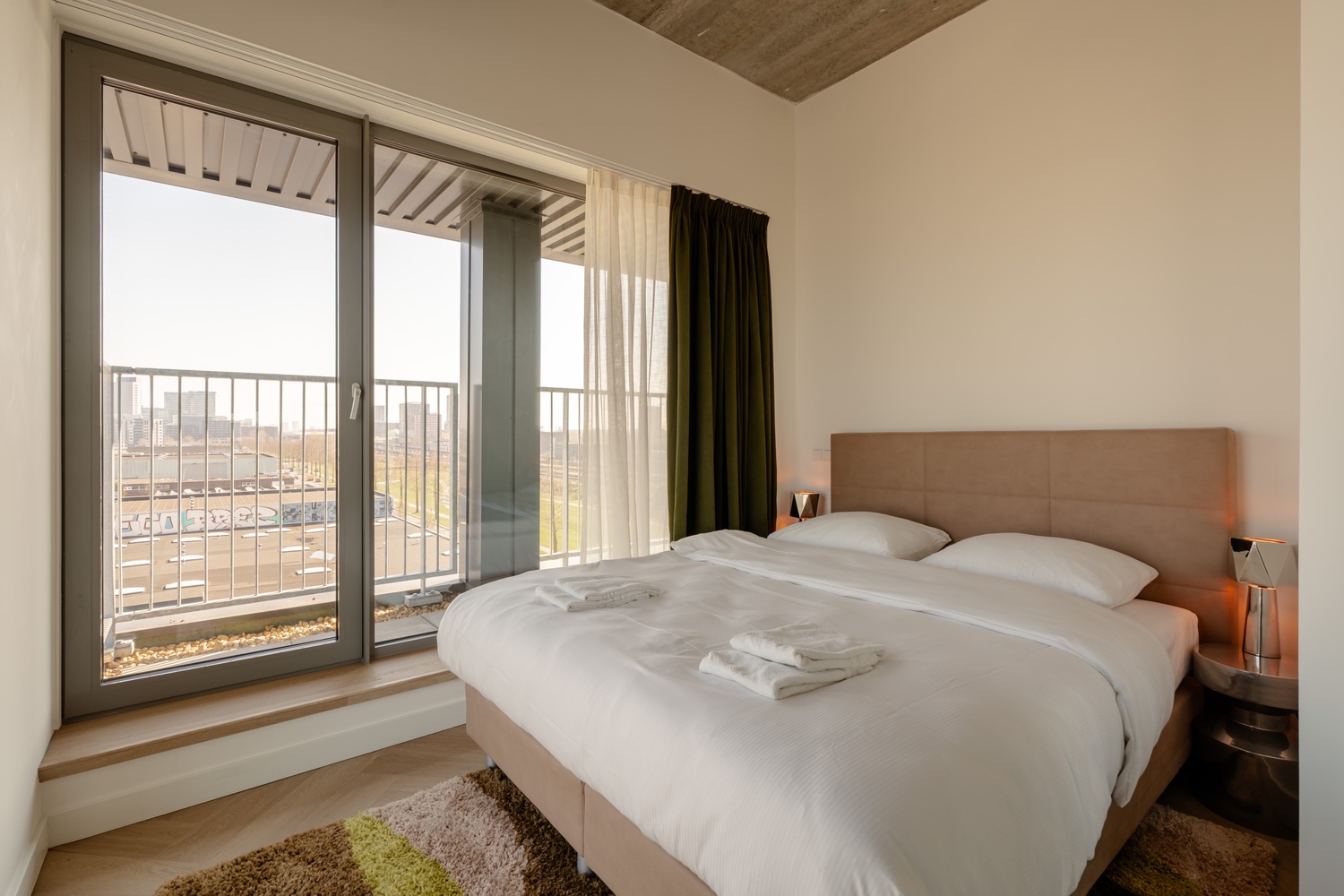 Bed bij de balkondeur van de Superior Studio with Balcony in Makerstoren, met uitzicht op de skyline van Amsterdam