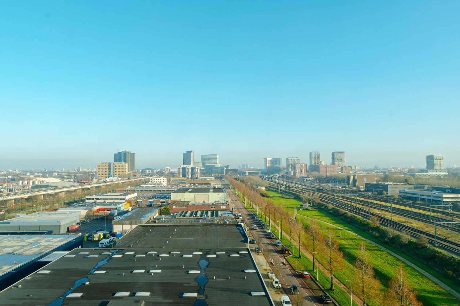 Uitzicht vanuit de Superior Studio in Makerstoren over groen, spoorlijn en de hoogbouw van Amsterdam