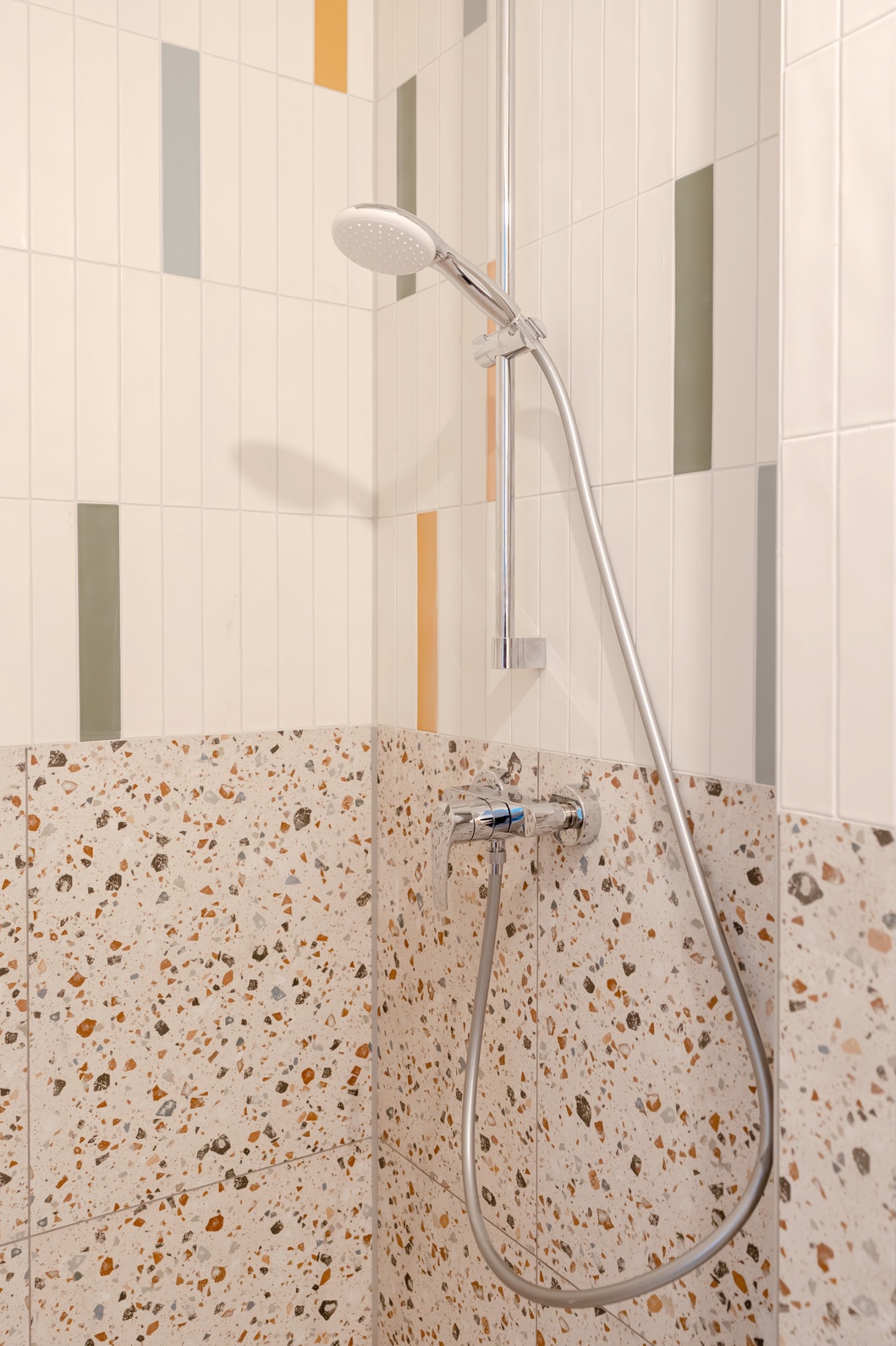 Douche met kleurrijke tegels en terrazzo in de en-suite badkamer van de Superior Studio, Makerstoren