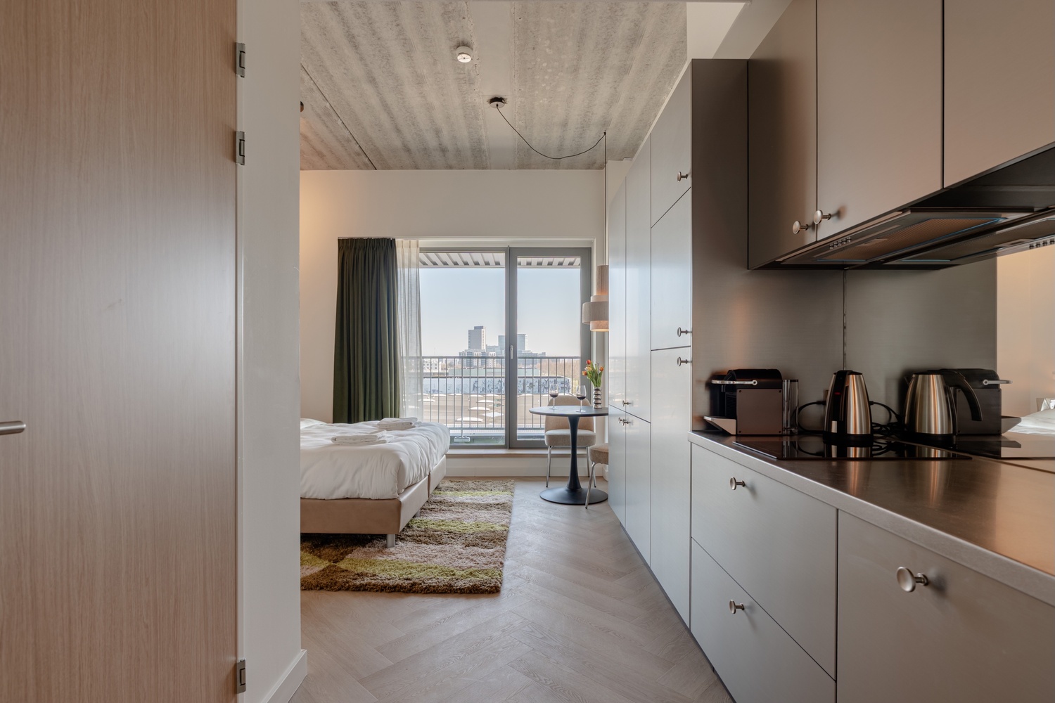 Standard Studio with Balcony in Makerstoren Amsterdam Sloterdijk met keuken, bed en balkondeur met uitzicht op de skyline