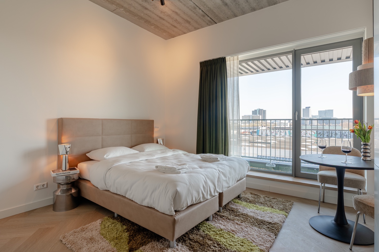 Tweepersoonsbed bij de balkondeur van de Standard Studio with Balcony, met uitzicht op de skyline van Amsterdam