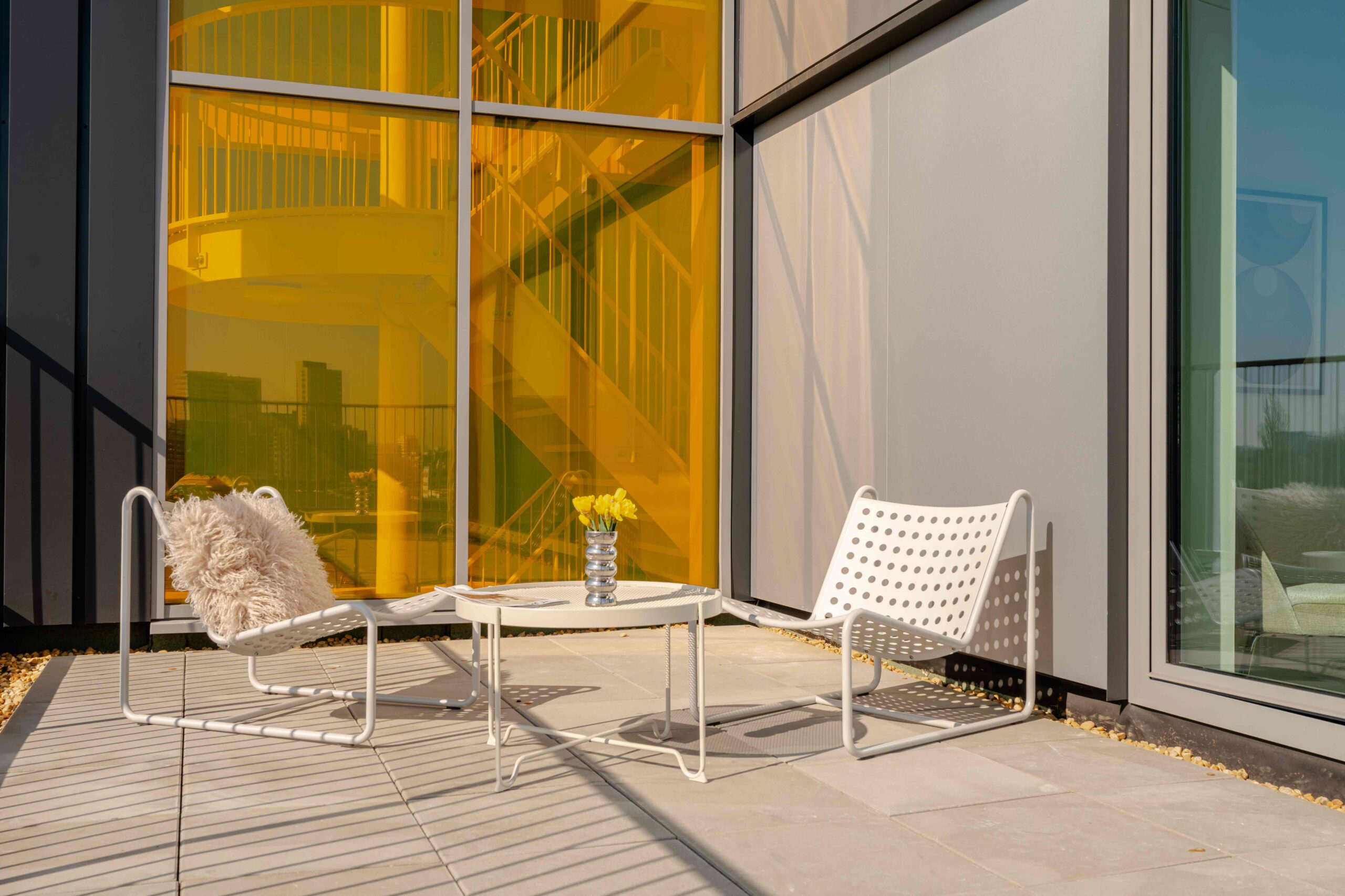 Terras short-stay appartement Amsterdam – Executive Corner met loungestoelen en gele glazen gevel